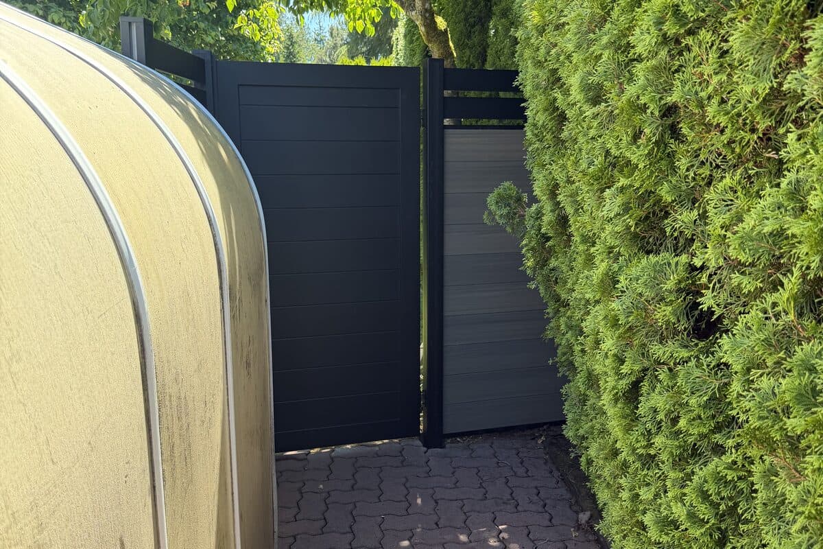 Finished black Proline gate beside backyard hedge